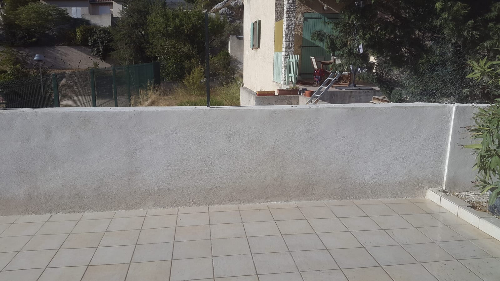 Terrasse carrelée et muret enduit finis, face à un cabanon provençal aux volets verts