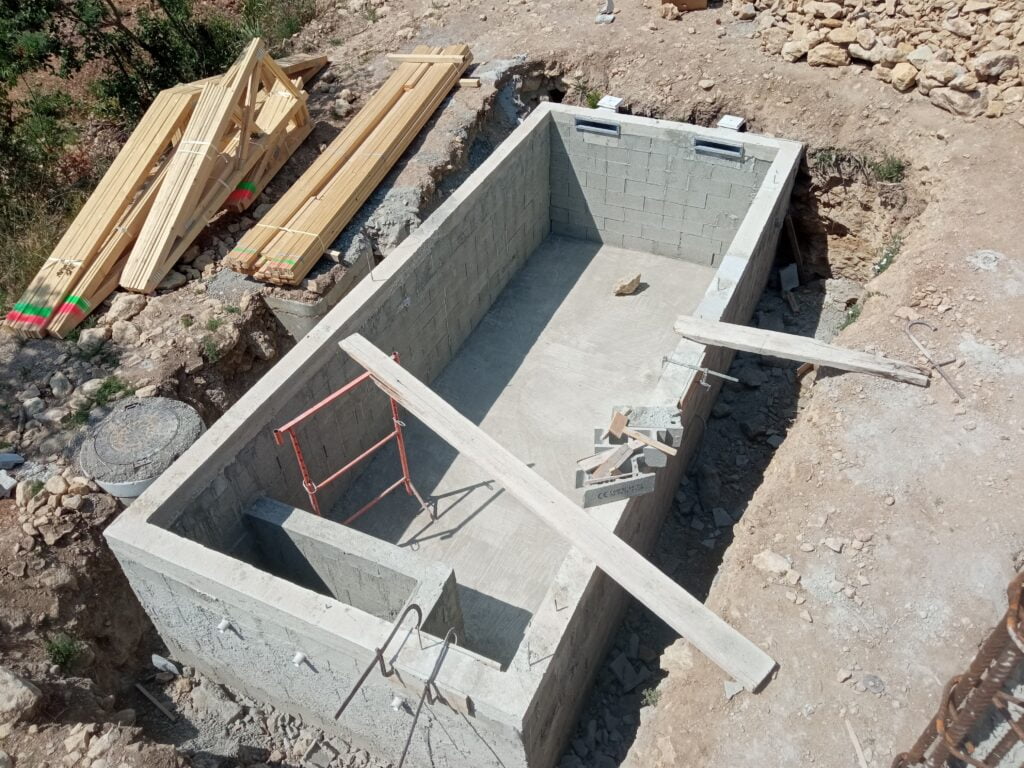 Bassin de piscine béton avec escalier et local technique intégré, charpente livrée en bord de chantier