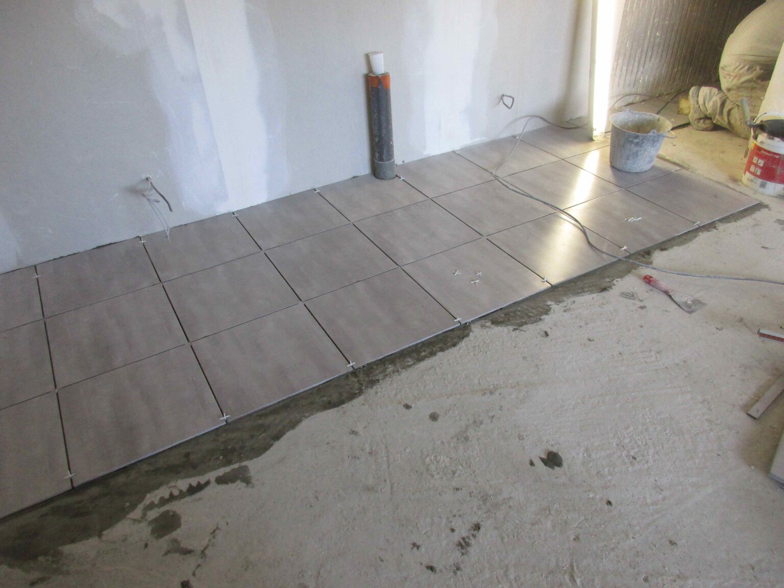 Pose de carrelage au sol en rénovation, attente d'évacuation en place contre le mur