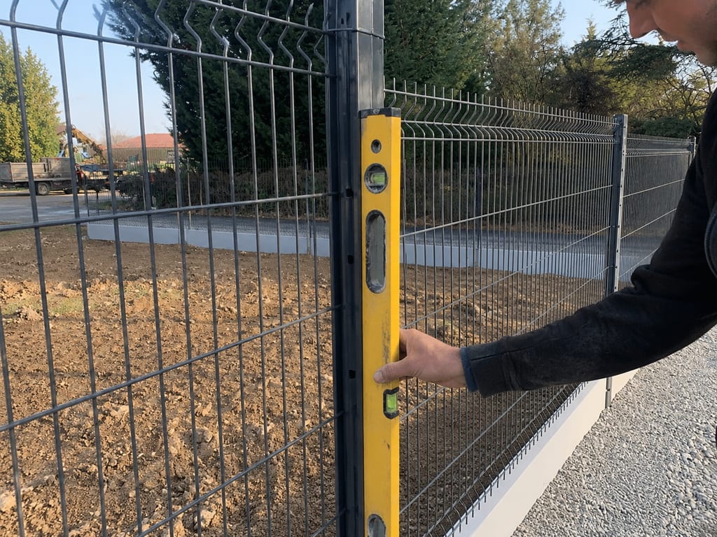 Contrôle du niveau d'un poteau de grillage rigide anthracite posé sur plaque de soubassement béton