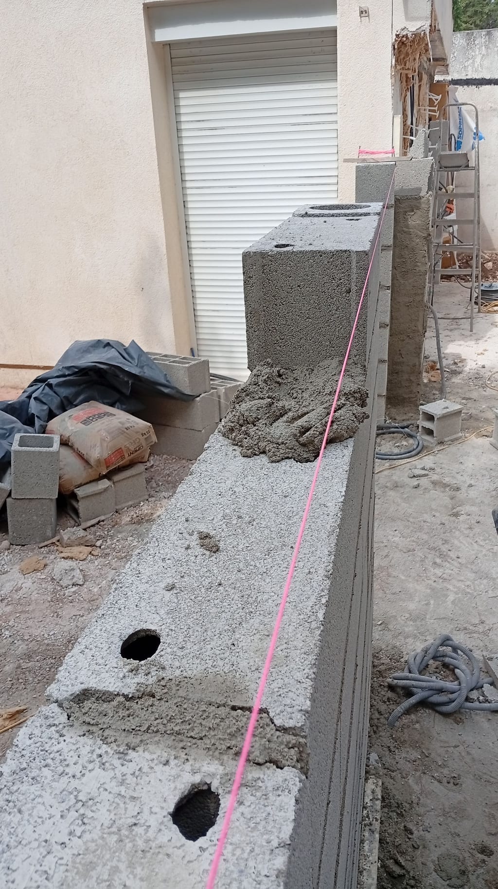 Mur d'agglo de l'extension monté au cordeau le long de la façade, sacs de ciment et cordeau rose — avenue du Lapin Blanc Marseille 13008, 15 juillet 2026